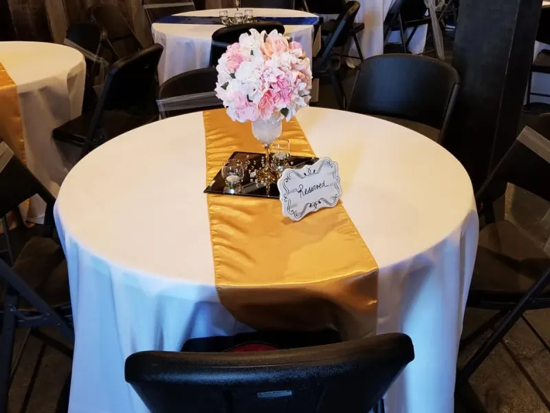 Reception table with white linens, a gold runner, and floral centerpiece